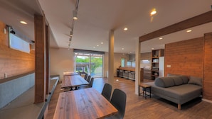 Un área de comedor moderna con mesas y sillas de madera, un sofá y una cocina al fondo.