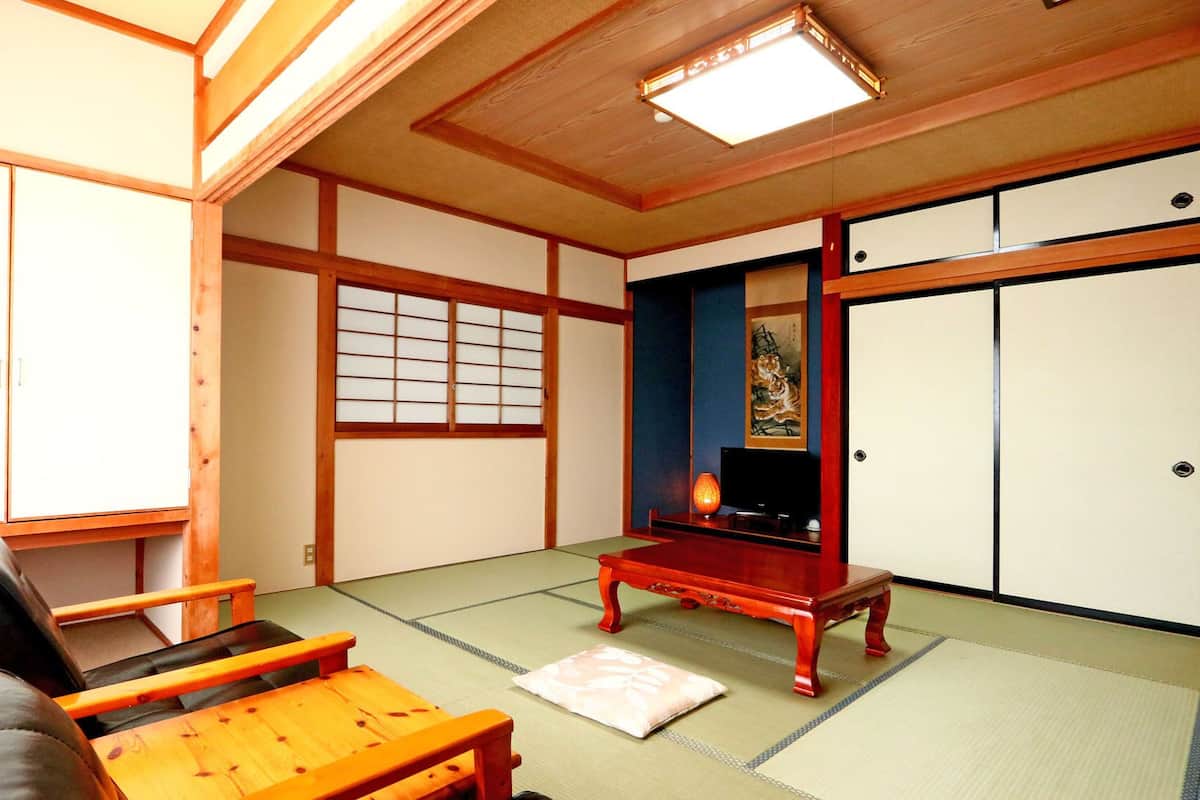 Ein traditioneller japanischer Raum mit Tatami-Bodenbelag, einem niedrigen Holztisch, einer Couch und Schiebetüren.