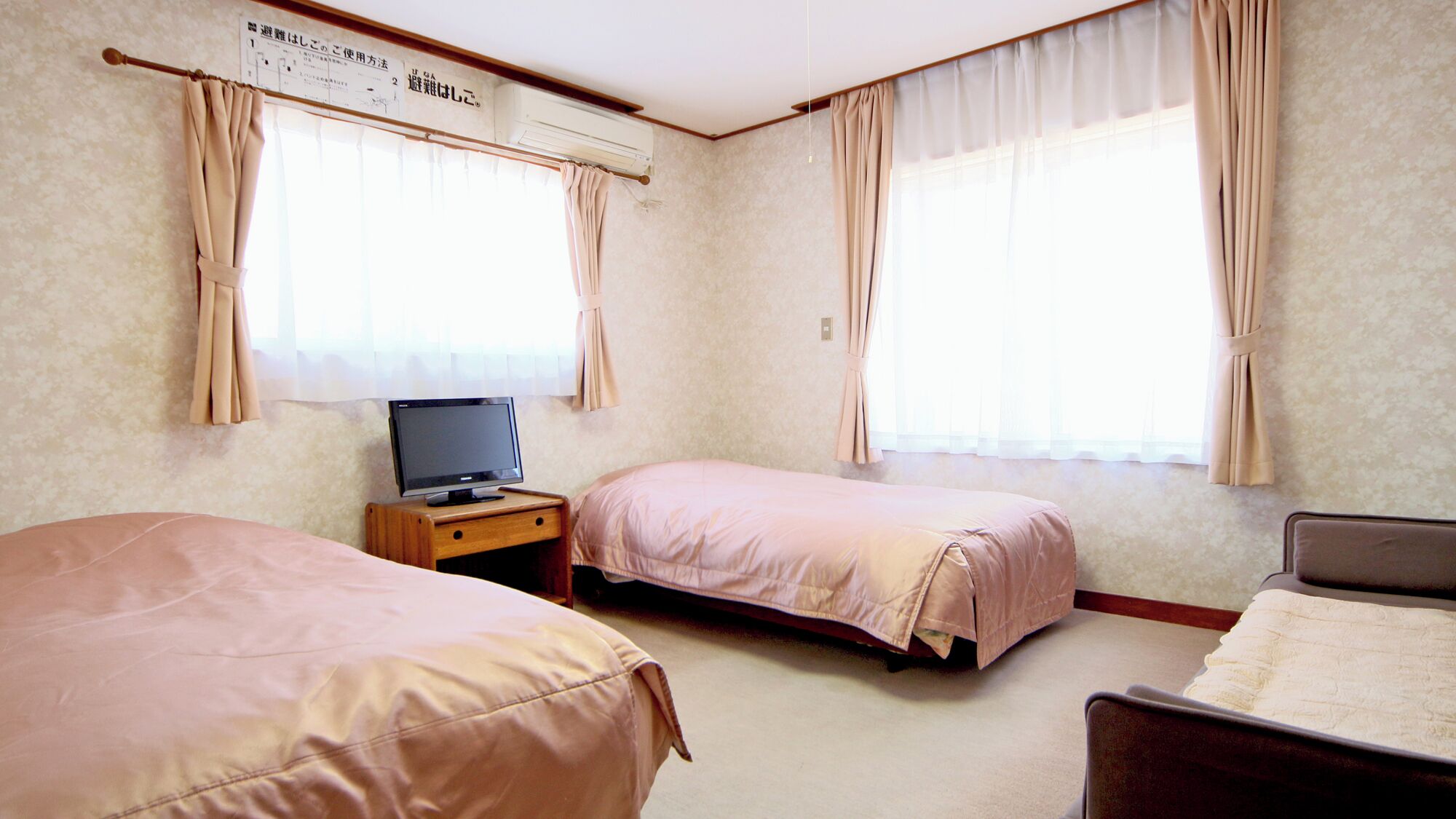 A hotel room with two beds, a TV on a wooden nightstand, and a window with curtains.