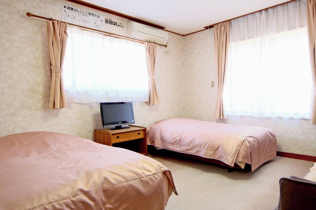 A hotel room with two beds, a TV on a wooden nightstand, and a window with curtains.