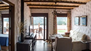 Una stanza con soffitto in legno, una zona pranzo con tavolo e sedie, un divano e vista su un paesaggio montuoso attraverso la porta aperta.