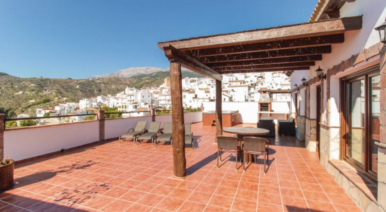 A terrace with a pergola, seating, and a view of a hillside town.