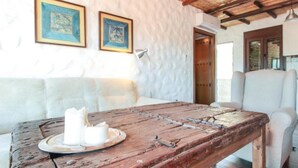 Un tavolo rustico in legno, con candele, un divano imbottito bianco e una poltrona bianca in una stanza con pareti strutturate e opere d'arte incorniciate.