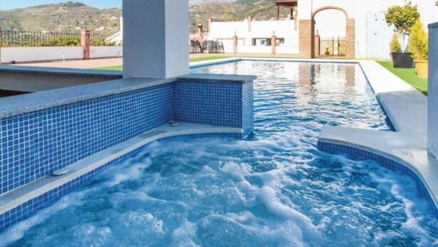 Zona idromassaggio con piscina, circondata da un edificio bianco e vista sulle colline.