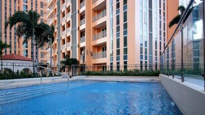 A swimming pool with clear blue water, surrounded by a high-rise building with balconies. - MaxStays Max Home at The Venice Residences (Taguig)