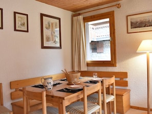 Un comedor acogedor con una mesa de madera y bancos, cuadros en las paredes y un ventanal con vistas a un edificio.