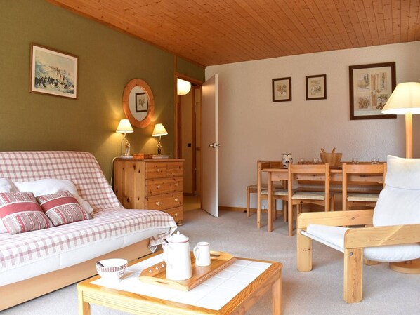 Un salon chaleureux avec un canapé, une table basse en bois, une table à manger avec des chaises et un buffet en bois agrémenté de lampes.