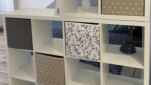 Una columna blanca d'emmagatzematge amb diversos compartiments, alguns amb motius florals i d'altres amb punts.