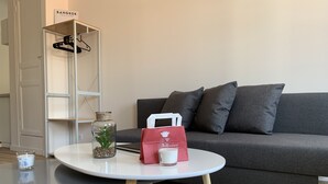 Un saló modern amb un sofà gris, una taula de centre blanca amb un bocal de vidre i una bossa vermella, i una catifa amb un disseny geomàtric.