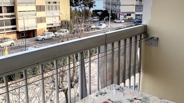 Un balcon avec une table, une balustrade et une vue sur un parking et des immeubles.