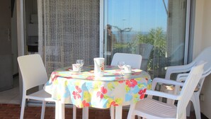 Eine Terrasse mit Tisch, bedeckt mit einer blumigen Tischdecke, umgeben von weißen Plastikstühlen.