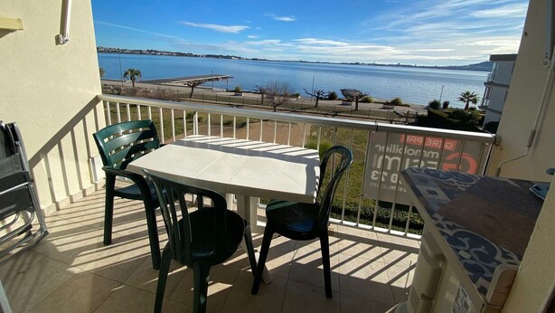 Un balcon avec une table et des chaises, donnant sur une étendue d’eau dont on aperçoit la côte au loin.