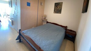 Une chambre à coucher avec un lit, un ventilateur de plafond, une étagère fixée au mur et une porte.