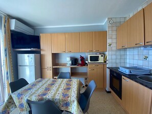 Una cocina compacta con armarios de madera, microondas, refrigerador y comedor con mesa y sillas.
