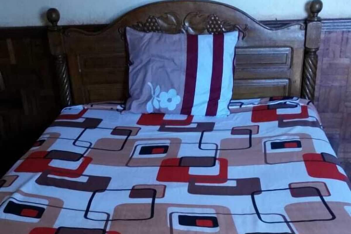 Un lit avec une couvre-lit à motifs géométriques, une tête de lit en bois et un coussin à motifs floraux.