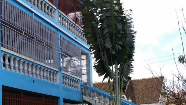 Un bâtiment à deux étages, à la façade bleue, doté d’un balcon avec des balustrades.