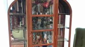 Une bibliothèque en bois avec des étagères en verre, remplie de divers objets, une chaise verte et un plancher en bois.