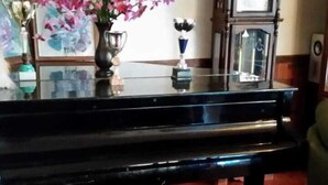 Un piano, un vase de fleurs, une horloge et une statue, le tout posé sur un plancher en bois.