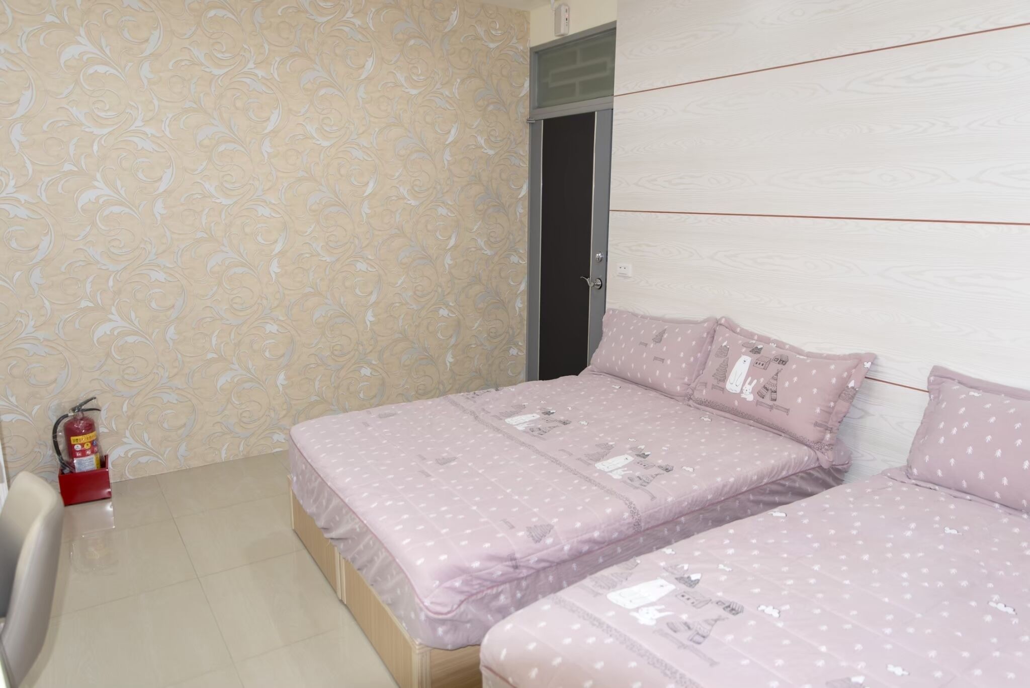 A bedroom with two beds, patterned wallpaper, a fire extinguisher, and a door.