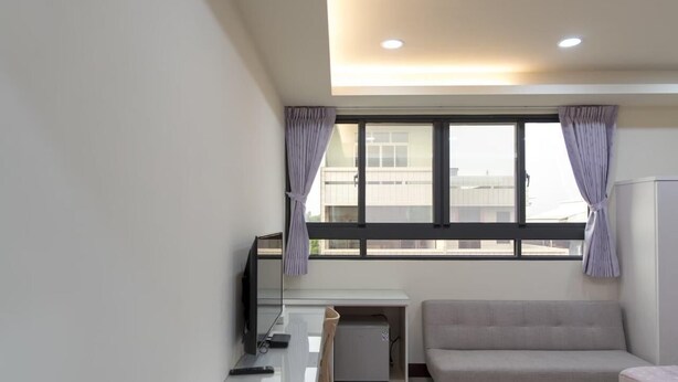A modern, well-lit room with a large window, a sofa, a desk with a computer, and a small cabinet. - Lvyou B&B (Tianwei)