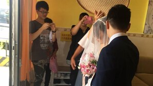 A wedding ceremony with a bride in a white dress and a groom in a dark suit. Guests are present, and a traditional round mat is visible. - Lvyou B&B (Tianwei)