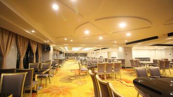 A spacious hotel conference room with rows of tables and chairs, a patterned carpet, and a modern ceiling design.