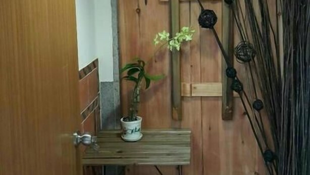 A wooden door with a small shelf holding a potted plant, a hanging light fixture, and a trash bin. - Joylin 3 Homestay (Jinning)