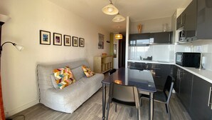 Een moderne keuken met donkere kastjes en een zwart aanrecht. Er staat een eettafel met vier stoelen. Een grijze bank met kleurrijke kussens staat tegen de muur.