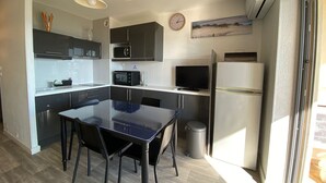Een moderne keuken met een eettafel, stoelen, een magnetron, een koelkast en een klok aan de muur.