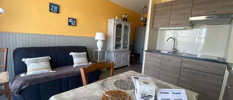 Un espacio habitable compacto con sofá, mesa de comedor y kitchenette.