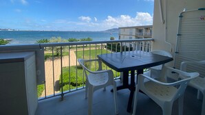 Uma varanda com mesa e cadeiras, com vista para um corpo de água e uma linha de costa distante.