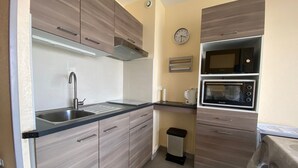 Uma cozinha compacta com pia, fogão, micro-ondas e um relógio na parede.