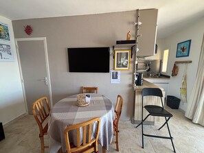A compact living space with a dining table, chairs, a kitchen area, and a flat-screen TV mounted on the wall.