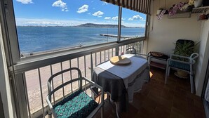 A balcony with a view of the sea, a table, chairs, and potted plants.