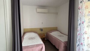 A small, simple room with two beds, a nightstand, and an air conditioning unit on the wall. - Charming air-conditioned studio, pets welcome in Balaruc-les-Bains (Balaruc-les-Bains)