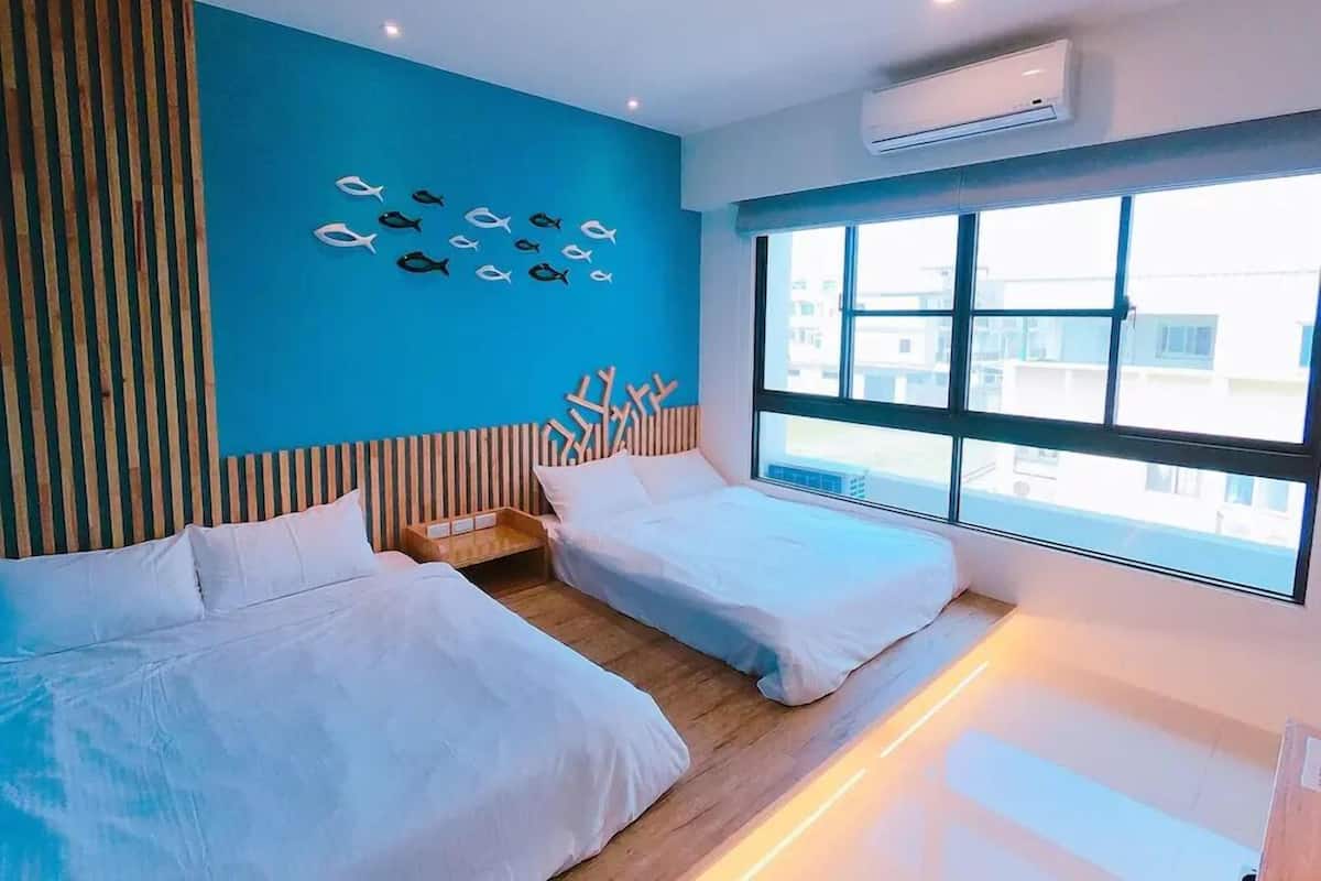 A modern hotel room with two beds, a large window, and a blue accent wall with fish decorations.