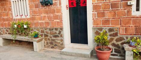 A brick building with a black door, potted plants, and a bench.
