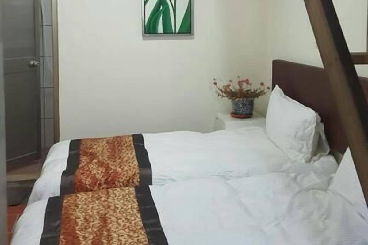 A bedroom with a bed, a framed picture of flowers on the wall, and a wooden staircase.