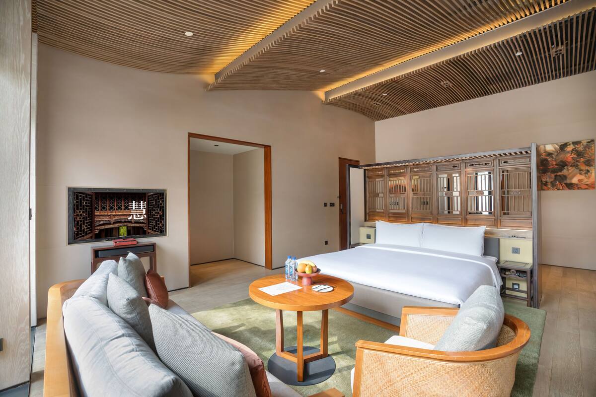 Une chambre d’hôtel moderne avec un grand lit, un plafond en bois, une table à manger et un canapé.