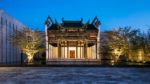 Un bâtiment traditionnel chinois, doté d’une architecture richement décorée, d’une porte centrale en bois et d’une cour intérieure plantée d’arbres.