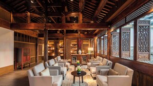 A spacious lobby with high ceilings and wooden beams, featuring a central seating area with sofas and a coffee table, surrounded by bookshelves and decorative screens. - Ahn Luh Zhujiajiao (Shanghai)