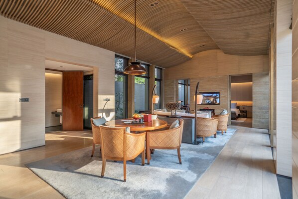 Un intérieur spacieux et moderne, avec un plafond en bois, un coin repas doté de chaises en osier et une cuisine avec une grande fenêtre.