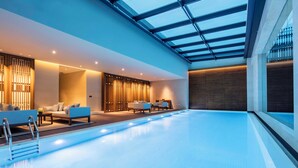 A modern indoor swimming pool with a glass ceiling, lounge area with sofas, and a wooden wall. - Ahn Luh Zhujiajiao (Shanghai)