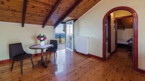 A spacious room with wooden flooring, a dining table with chairs, a vase with flowers, and a view to the outside.
