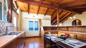 A dining area with a wooden table set for two, a kitchen with a sink and cabinets, and a view of the sea through a window.