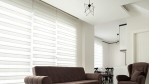 A modern living room with a brown sofa, a matching armchair, and a dining area in the background.