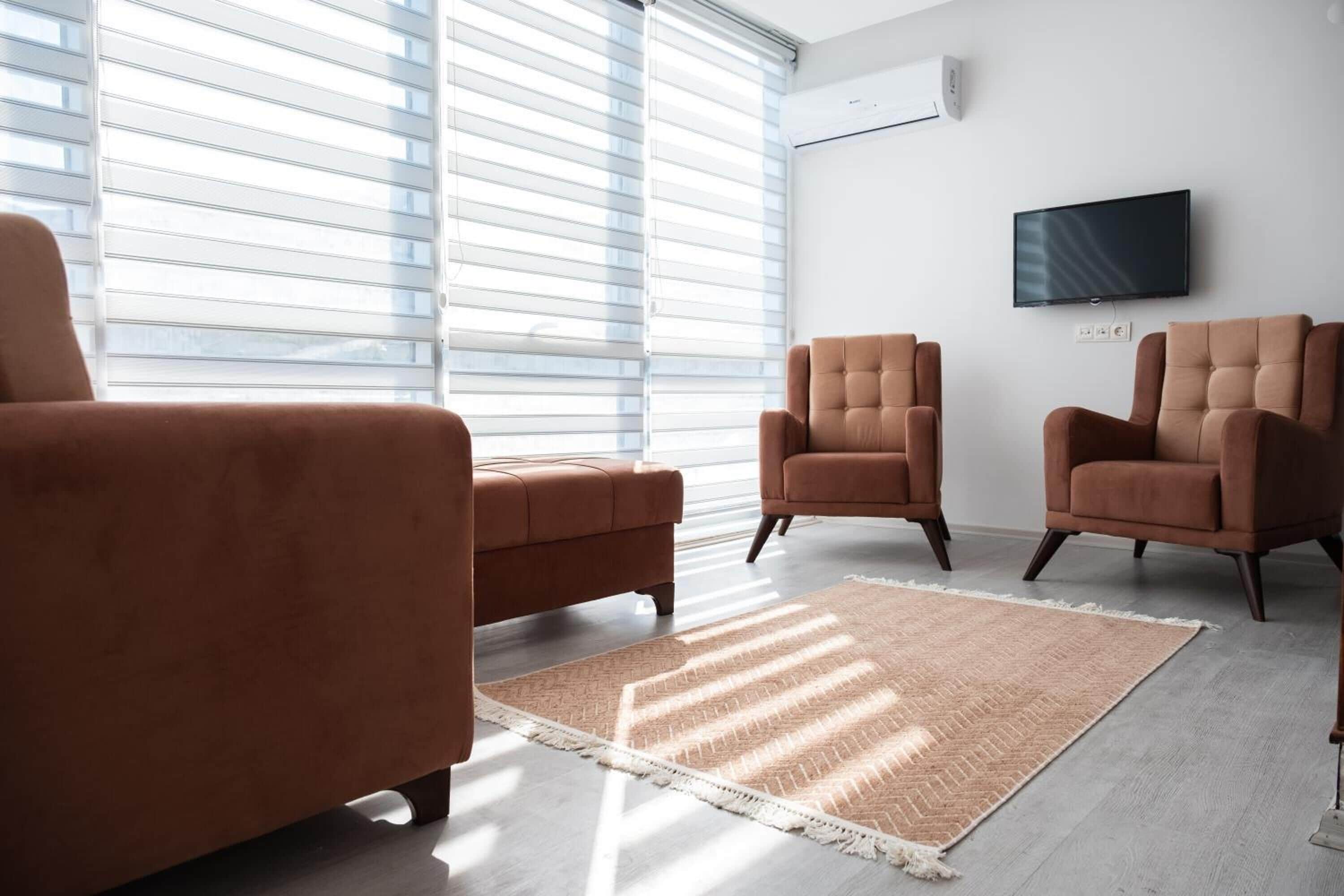 A living room with a large window, a flat-screen TV, and three brown armchairs.