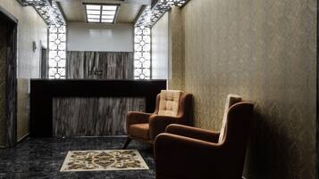 A lobby with a reception desk, two armchairs, a patterned rug, and a decorative ceiling.