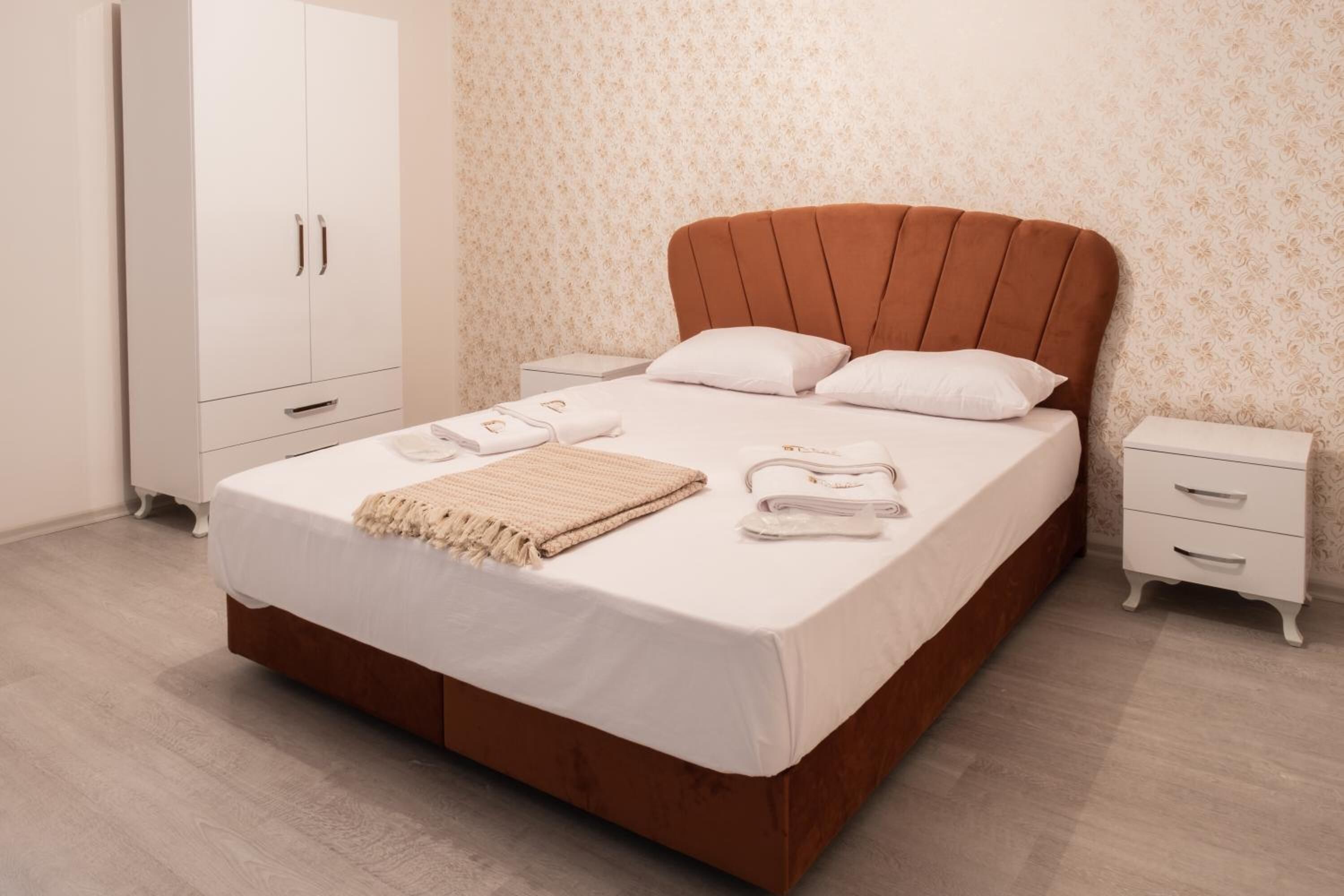 Una cama bien tendida con un cabecero marrón, ropa de cama blanca y dos mesitas de noche con lámparas.