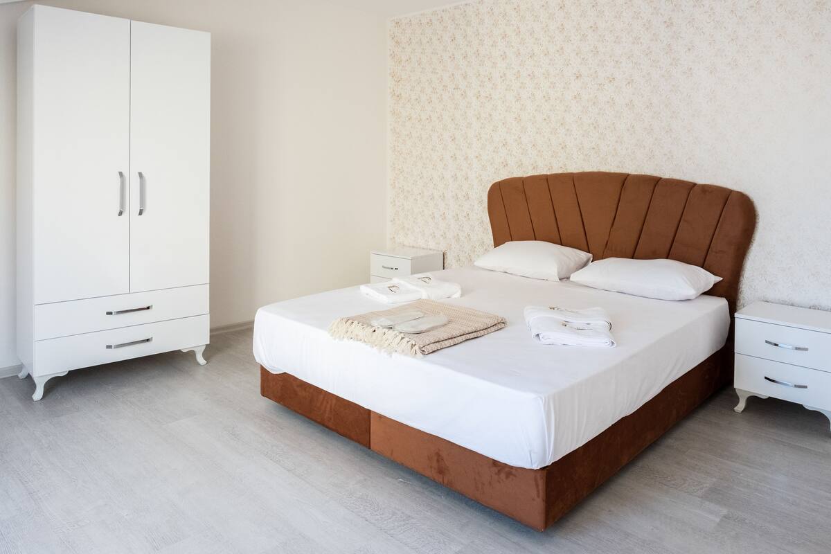 A bedroom with a large bed, a wardrobe, a nightstand, and a wall with a floral pattern.